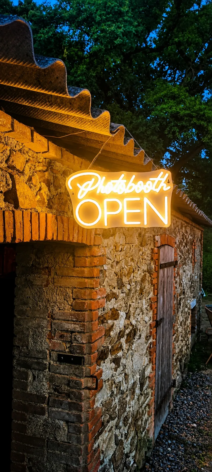 Enseigne lumineuse « Photobooth open » à l'entrée du bâtiment de pierre, à la tombée du soir