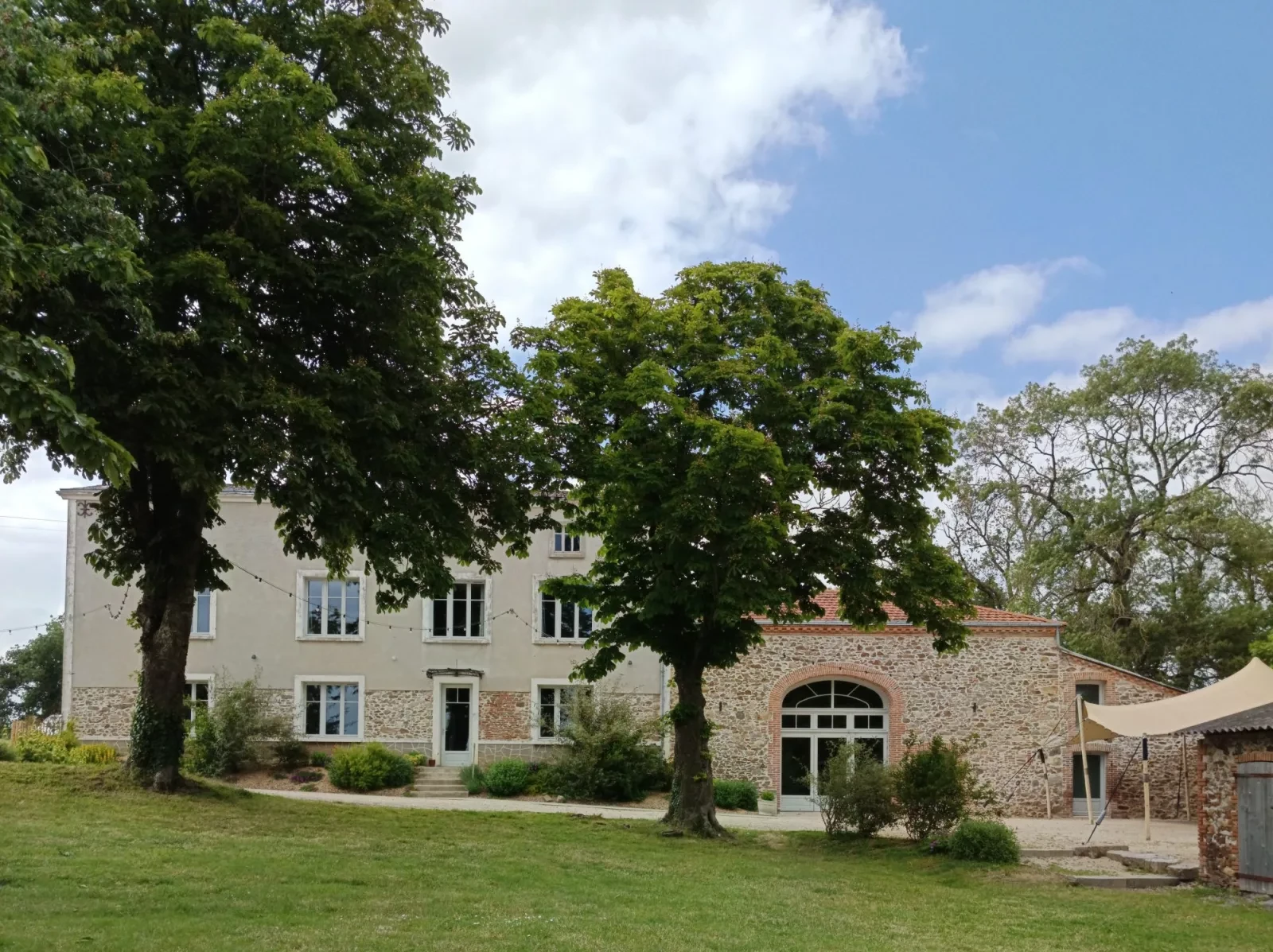 Le gîte et la salle vus de la pelouse, sous deux grands marronniers