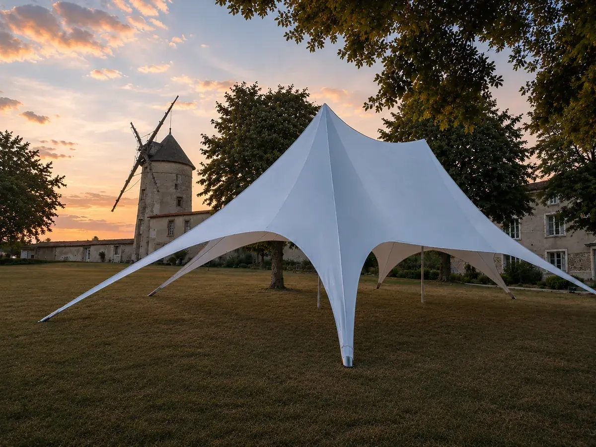 La tente étoile blanche dressée seule sur la pelouse du parc, le moulin en pierre derrière elle au coucher du soleil