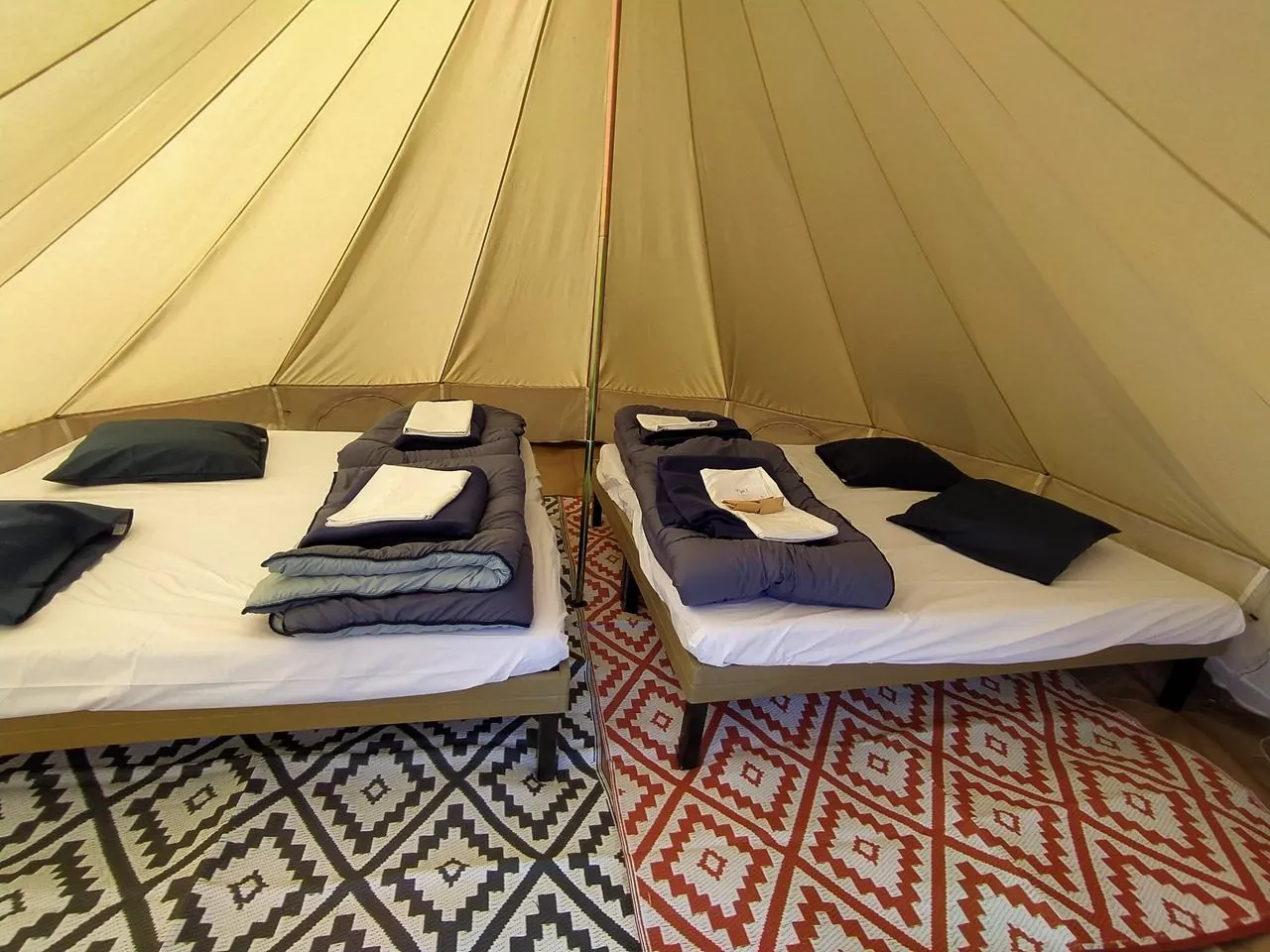 L'intérieur d'une tente : deux lits sur sommier, matelas blancs, couettes et oreillers posés, tapis au sol